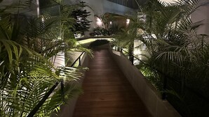 Un escalier entouré d’une végétation luxuriante, menant à un bâtiment doté de grandes fenêtres et d’un design moderne.