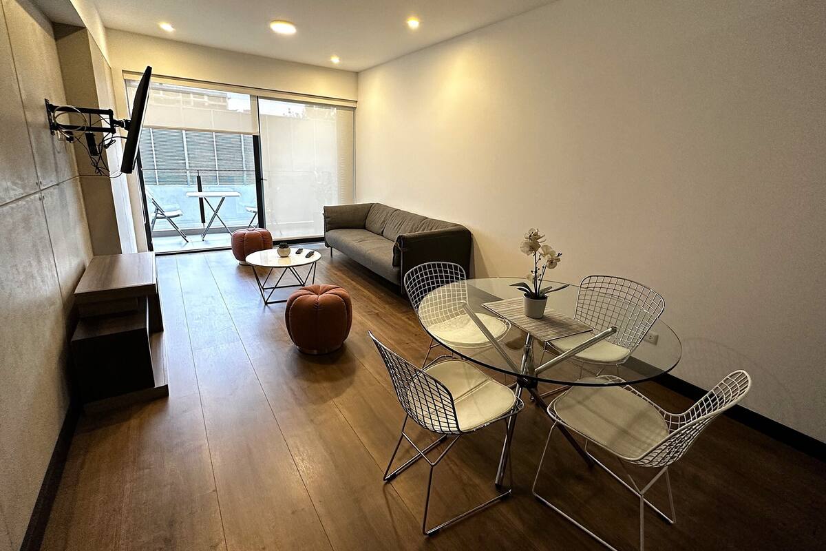 Een moderne woonkamer met een glazen eettafel, stoelen van metaaldraad, een bank en een salontafel met een potplant.
