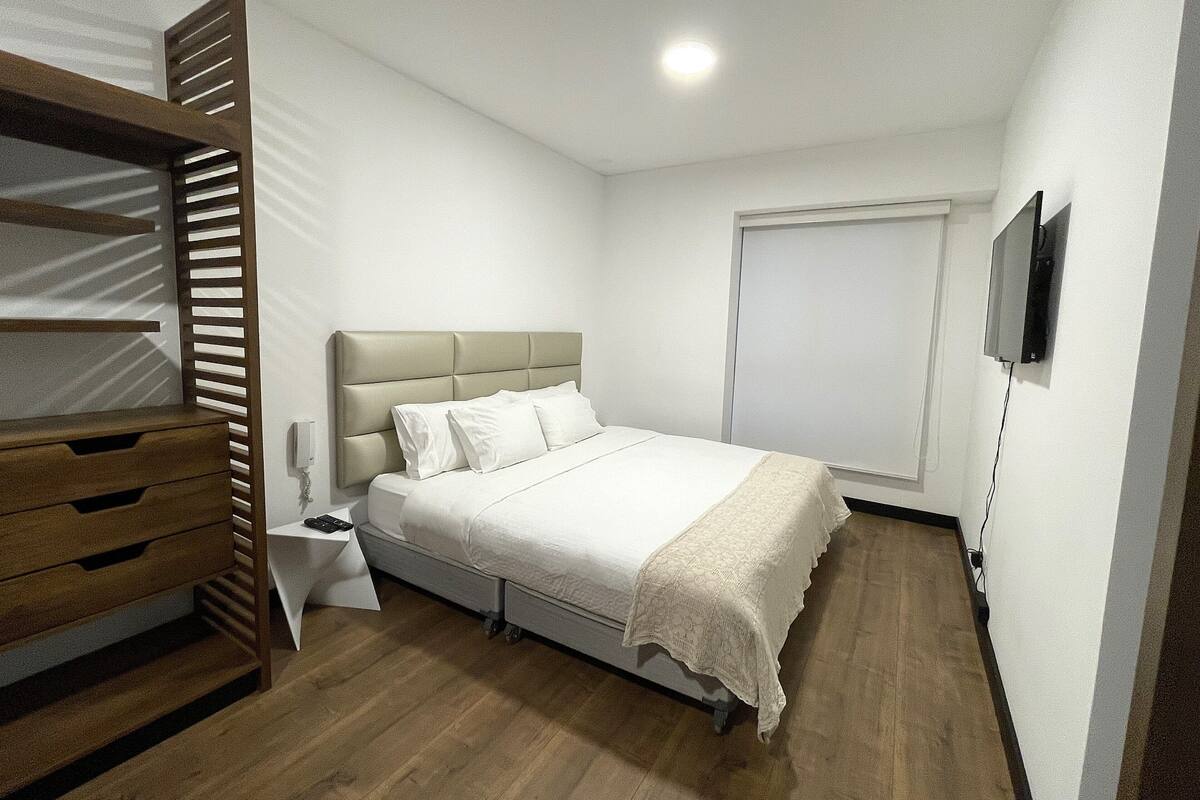 Een slaapkamer met een bed, een houten garderobe, nachtkastje en een aan de muur bevestigde televisie.
