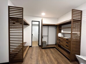 Un dressing accessible sans porte, doté d’étagères en lattes de bois, d’une porte de placard miroir et d’une petite poubelle.