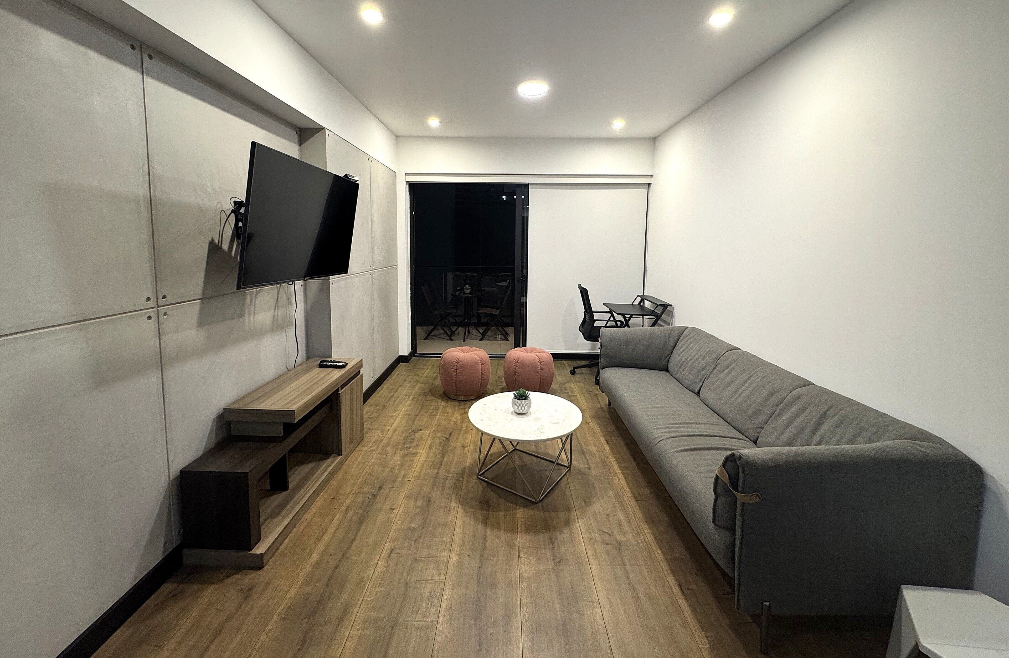 A modern living room with a grey sofa, a round coffee table, a flat-screen TV mounted on the wall, and a wooden bench.