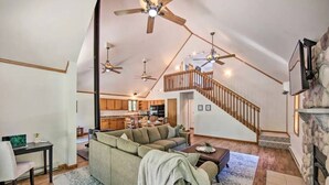 A spacious living area with a high ceiling, a wooden staircase, and a kitchen in the background.