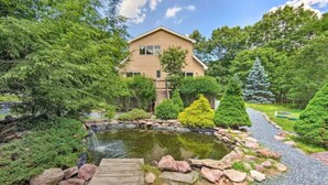 A house surrounded by a garden with a pond, a wooden deck, and a variety of trees and shrubs.