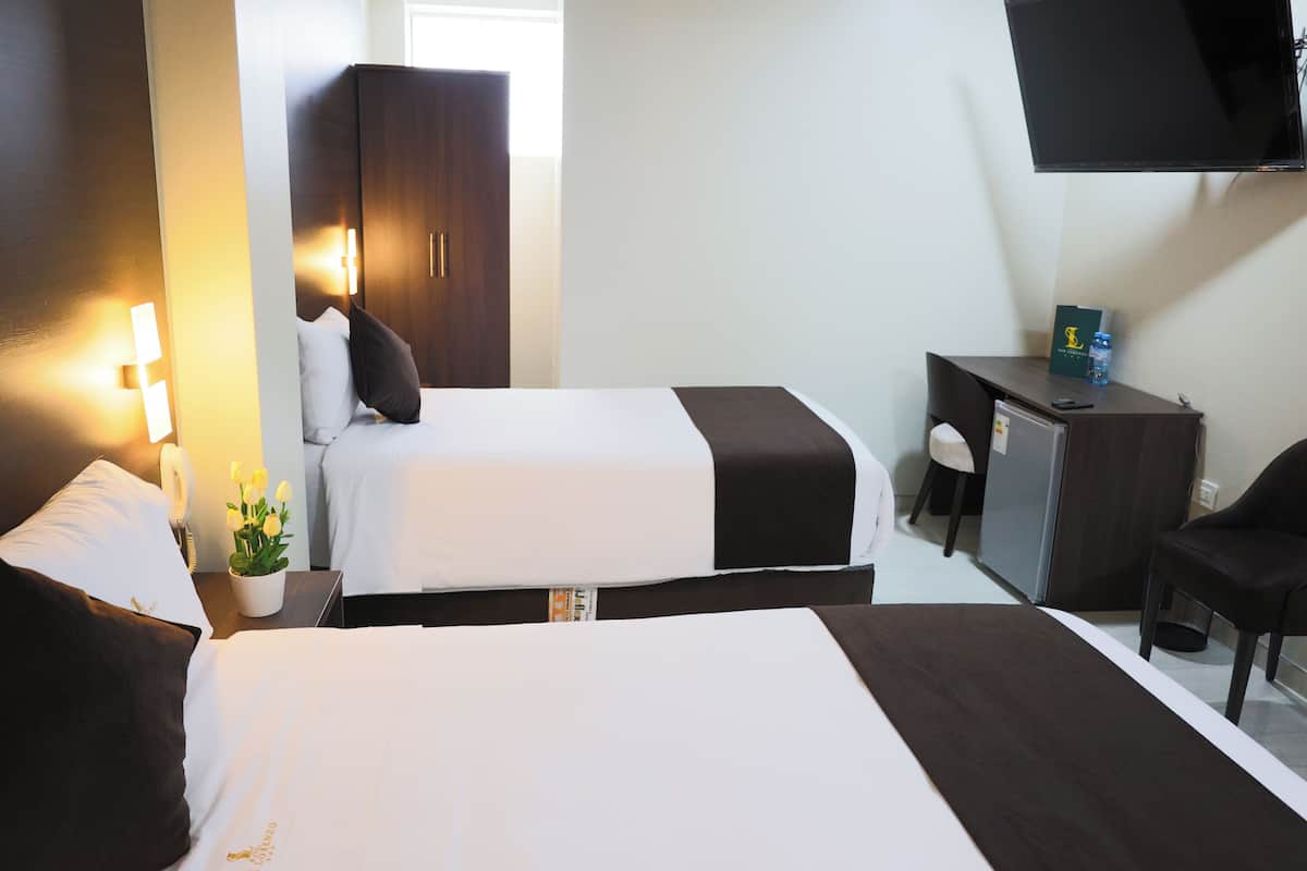 A hotel room with two beds, a desk, a chair, a wardrobe, and a flat-screen TV.