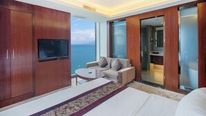 A hotel room with a large bed, a TV, a sofa, and a view of the ocean. - Haibaina Hotel (Huidong)