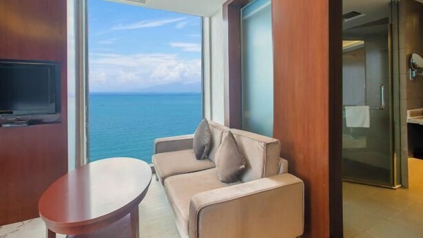 A balcony with a view of the ocean, a sofa, a small table, and a television. - Haibaina Hotel (Huidong)