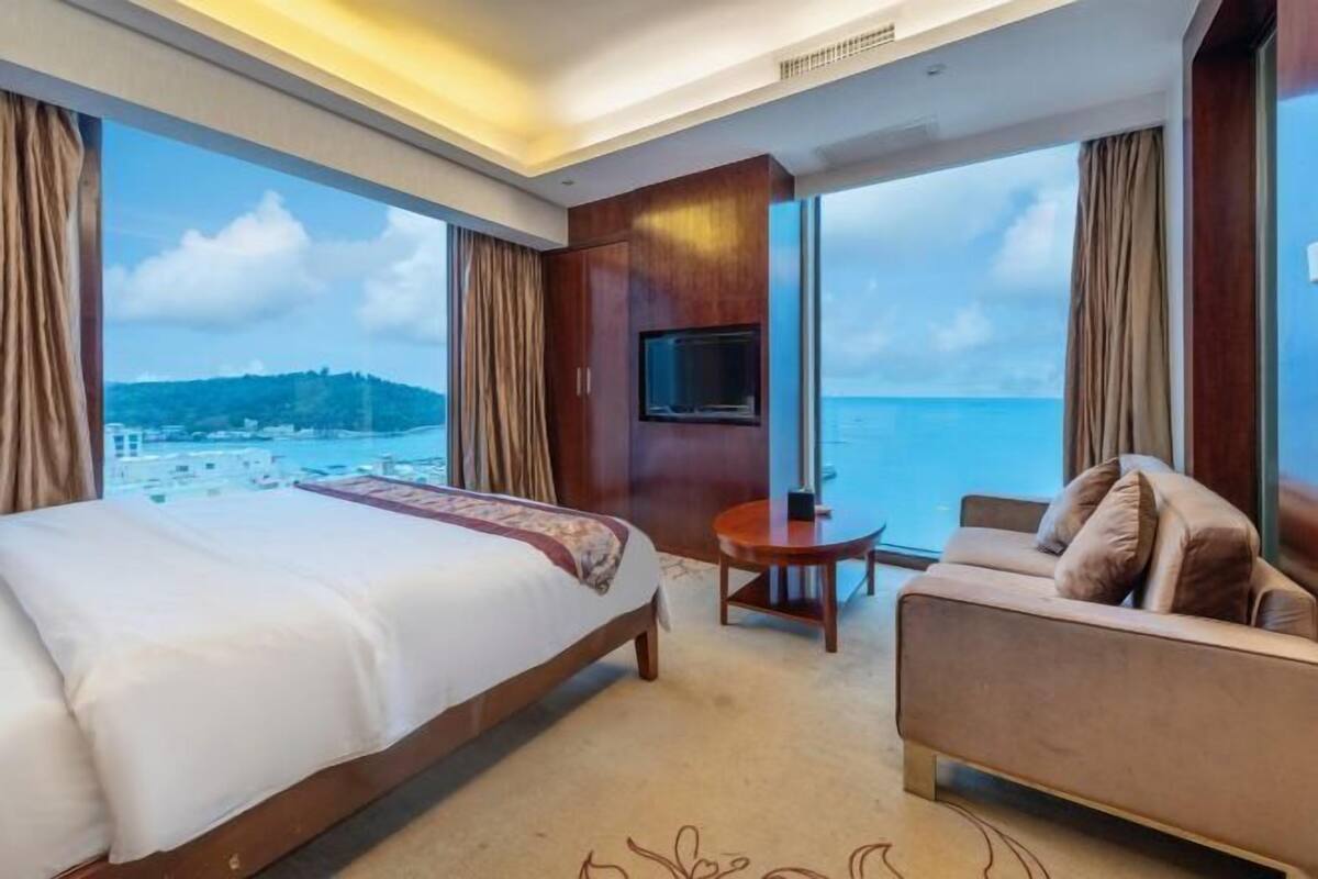 A hotel room with a bed, a sofa, a TV, and a view of the sea.