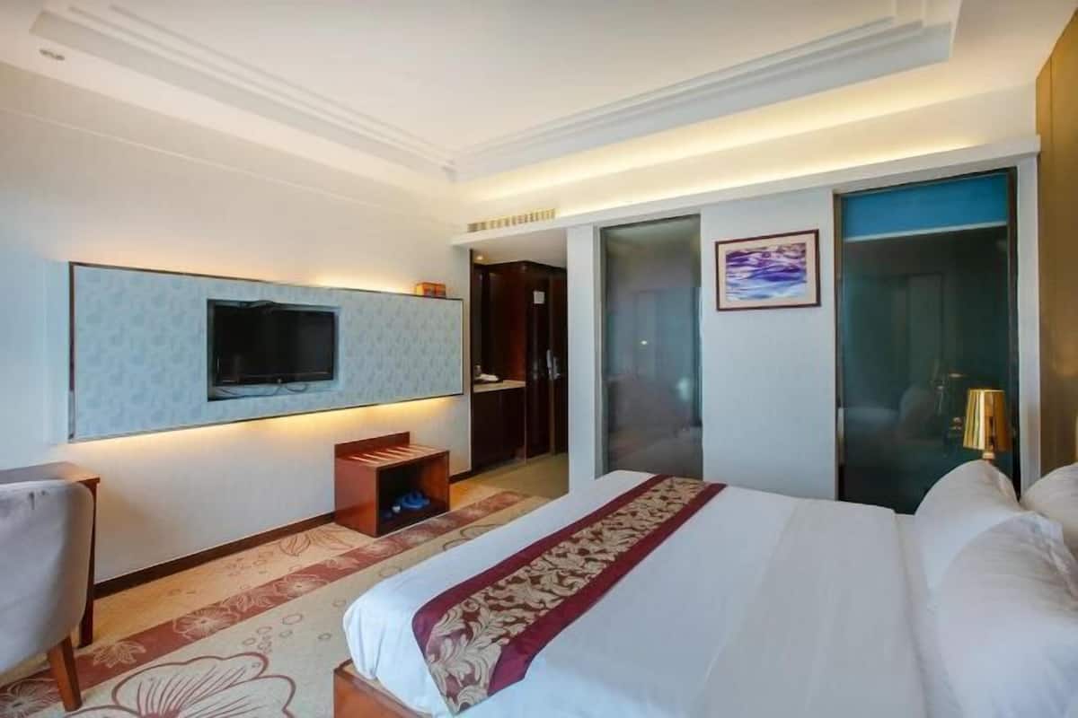 A hotel room with a bed, a TV mounted on the wall, a desk, a chair, and a door leading to a bathroom.