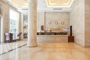 A hotel reception area with a marble floor, a reception desk, a large pillar, and framed pictures on the wall. - Haibaina Hotel (Huidong)