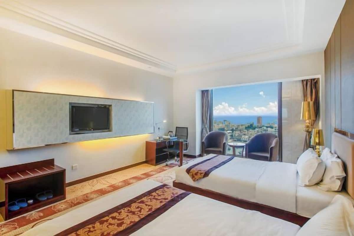 A hotel room with two beds, a TV, a desk with a computer, a chair, and a view of a cityscape.