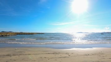 Una playa con un muelle que se adentra en el agua, cielos despejados y mar en calma.