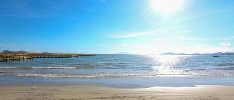 Ein Strand mit einem Steg, der ins Wasser führt, bewölkter Himmel und ruhiges Meer.
