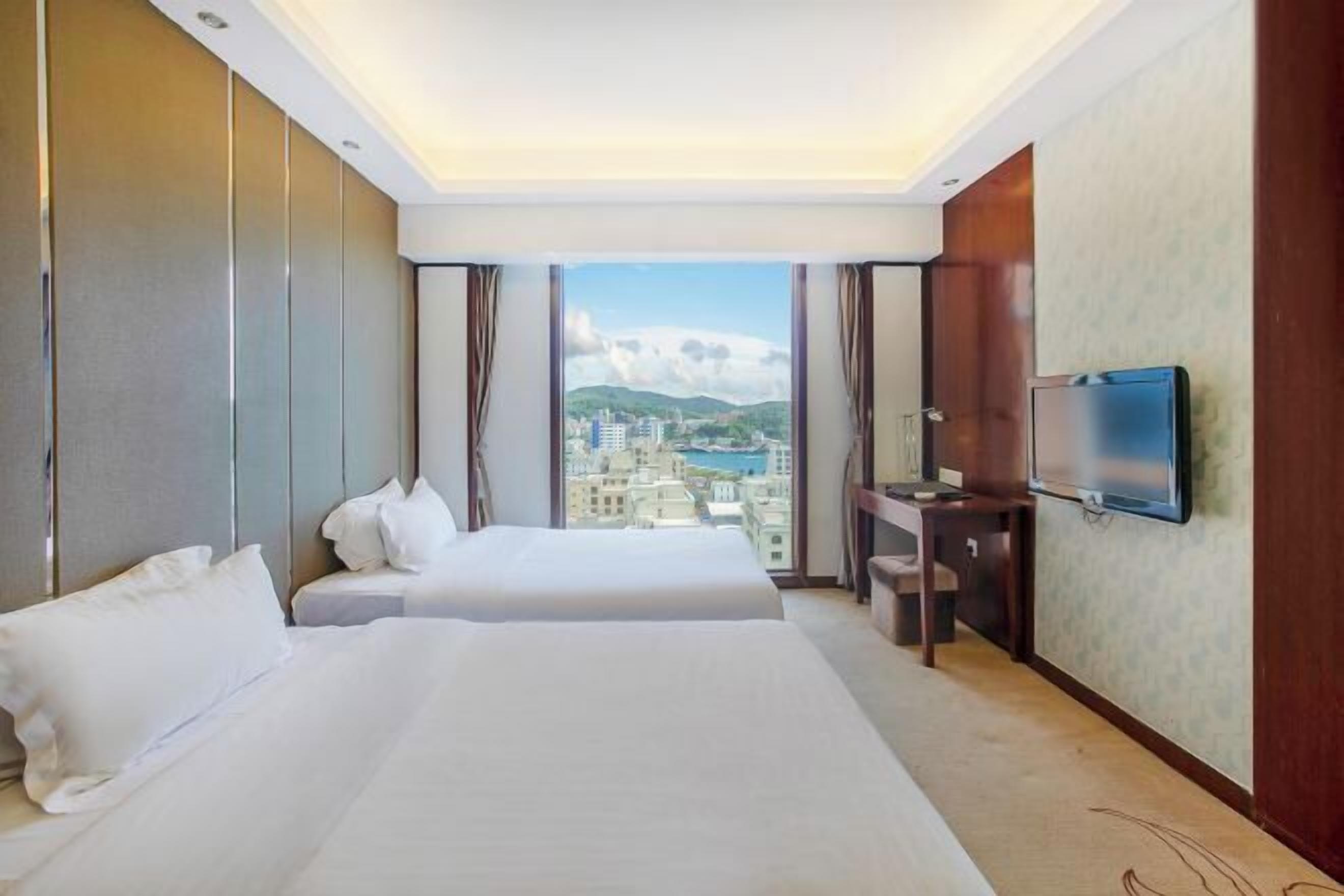 Ein Hotelzimmer mit zwei Betten, einem Schreibtisch, einem Fernseher und Blick auf die Stadt.
