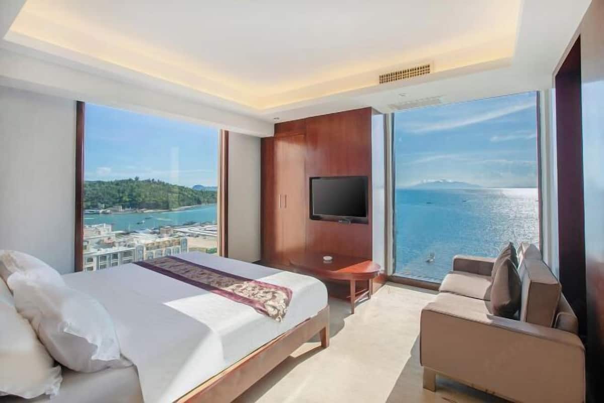 A hotel room with a bed, a TV, a sofa, and a balcony with a view of the sea.