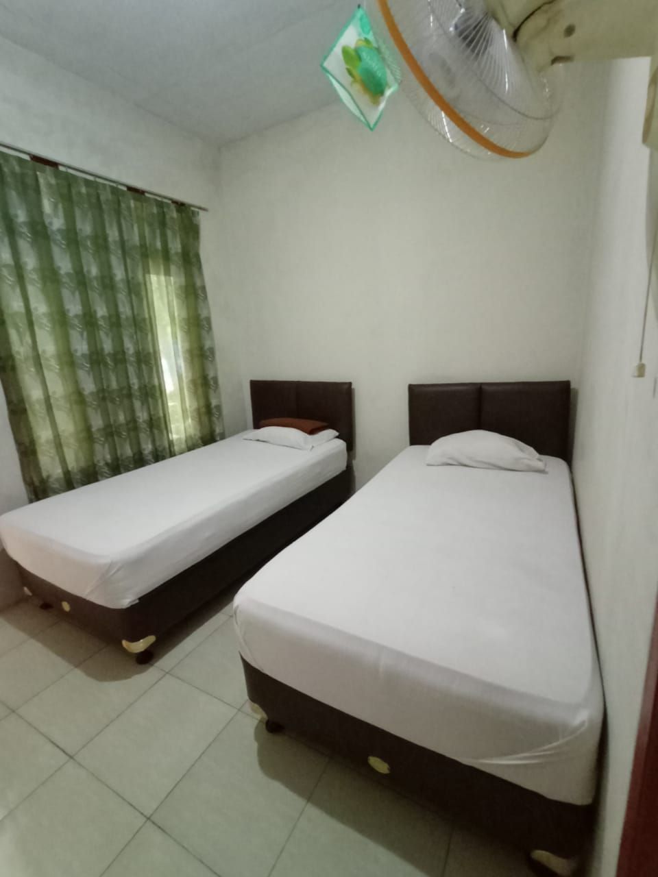 A room with two single beds, a ceiling fan, and a window with green curtains.