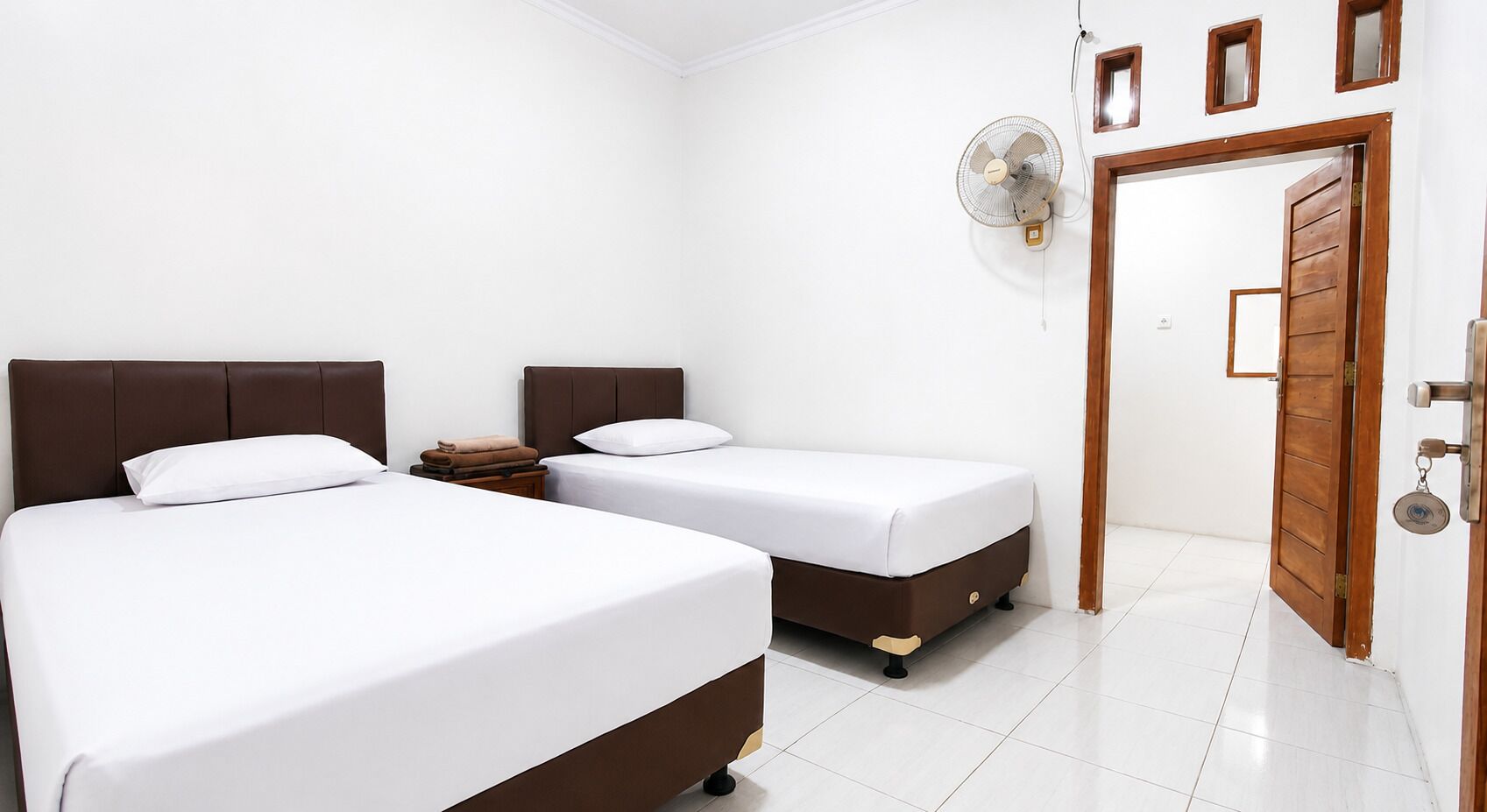 Ein Schlafzimmer mit zwei Betten, einem Wandventilator und einer Holztür.