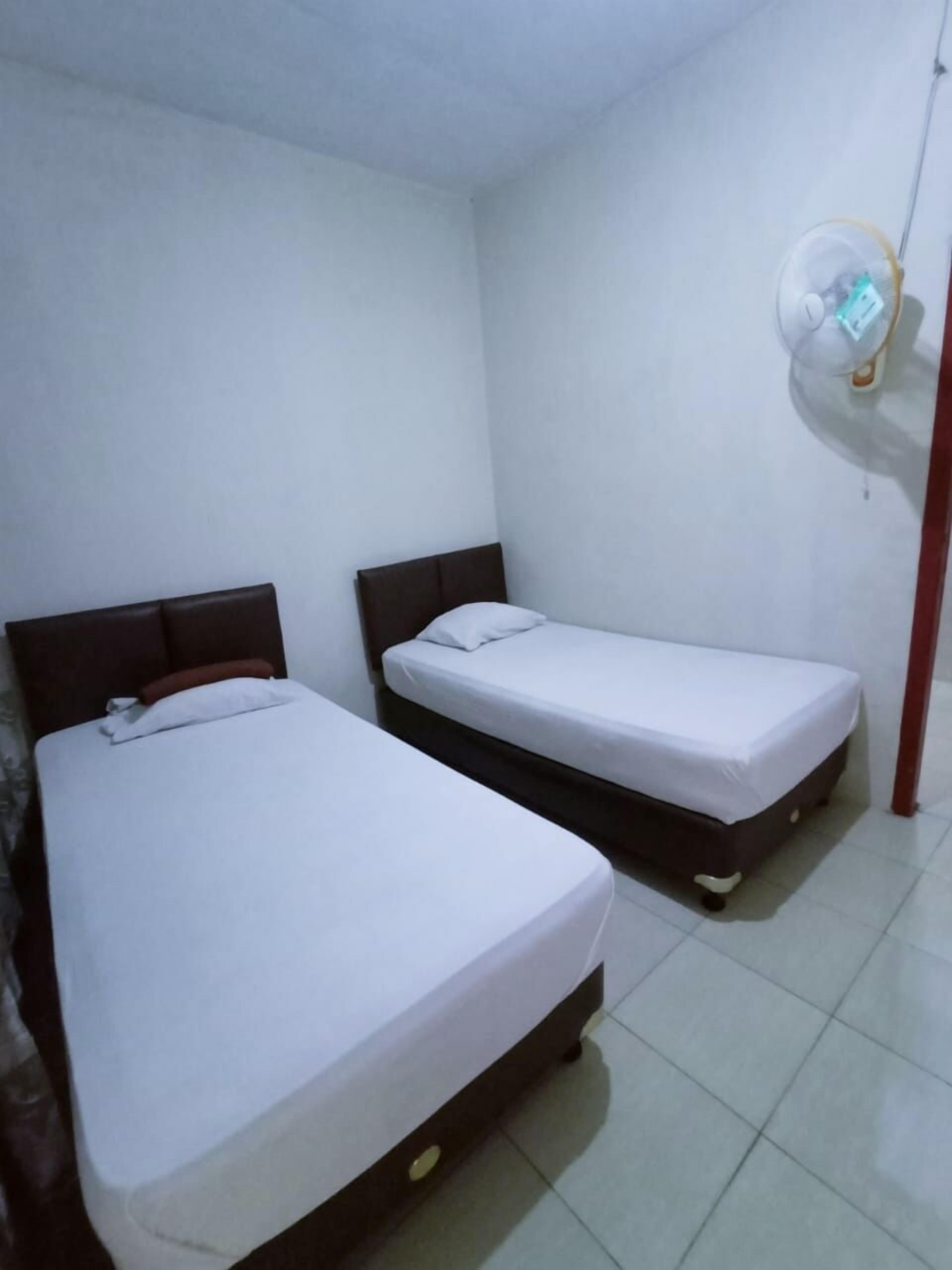 A small, clean room with two single beds, a white wall, and a ceiling fan.