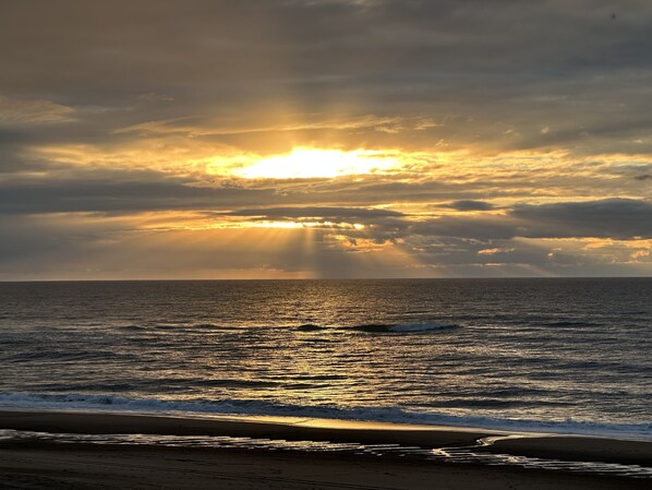 Una playa con el sol poniéndose sobre el océano, creando un ambiente tranquilo.