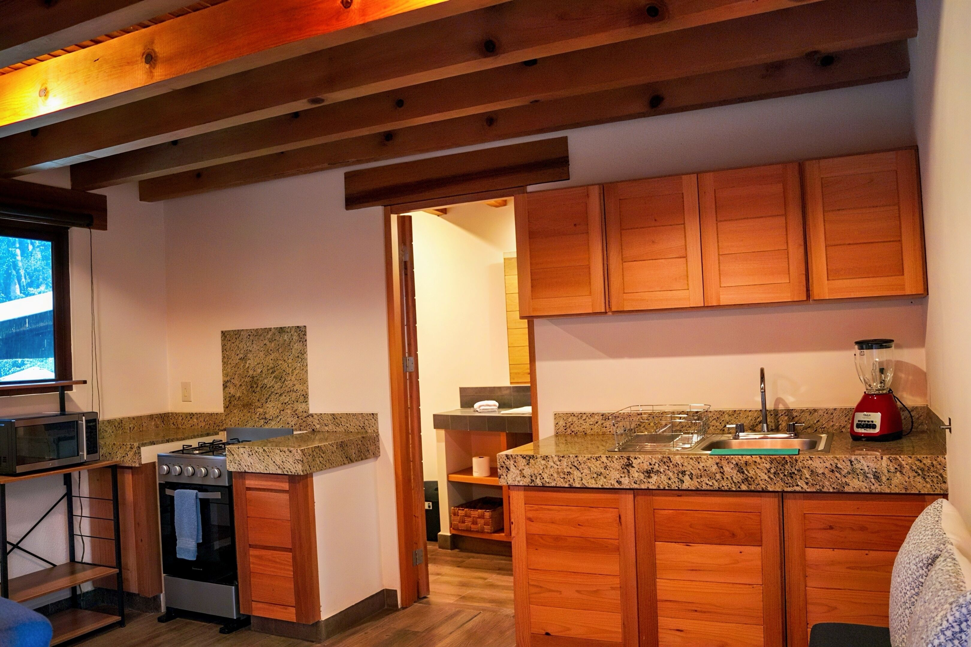 A compact kitchen with wooden cabinets, a granite countertop, a stove, and a microwave.