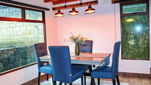 Un comedor con una mesa, sillas, un jarrón con flores e iluminación colgante.