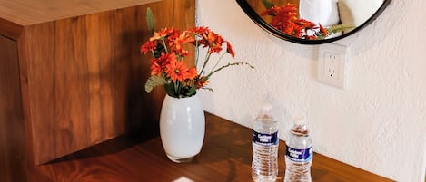 A wooden desk with a mirror, a vase with flowers, and two water bottles.