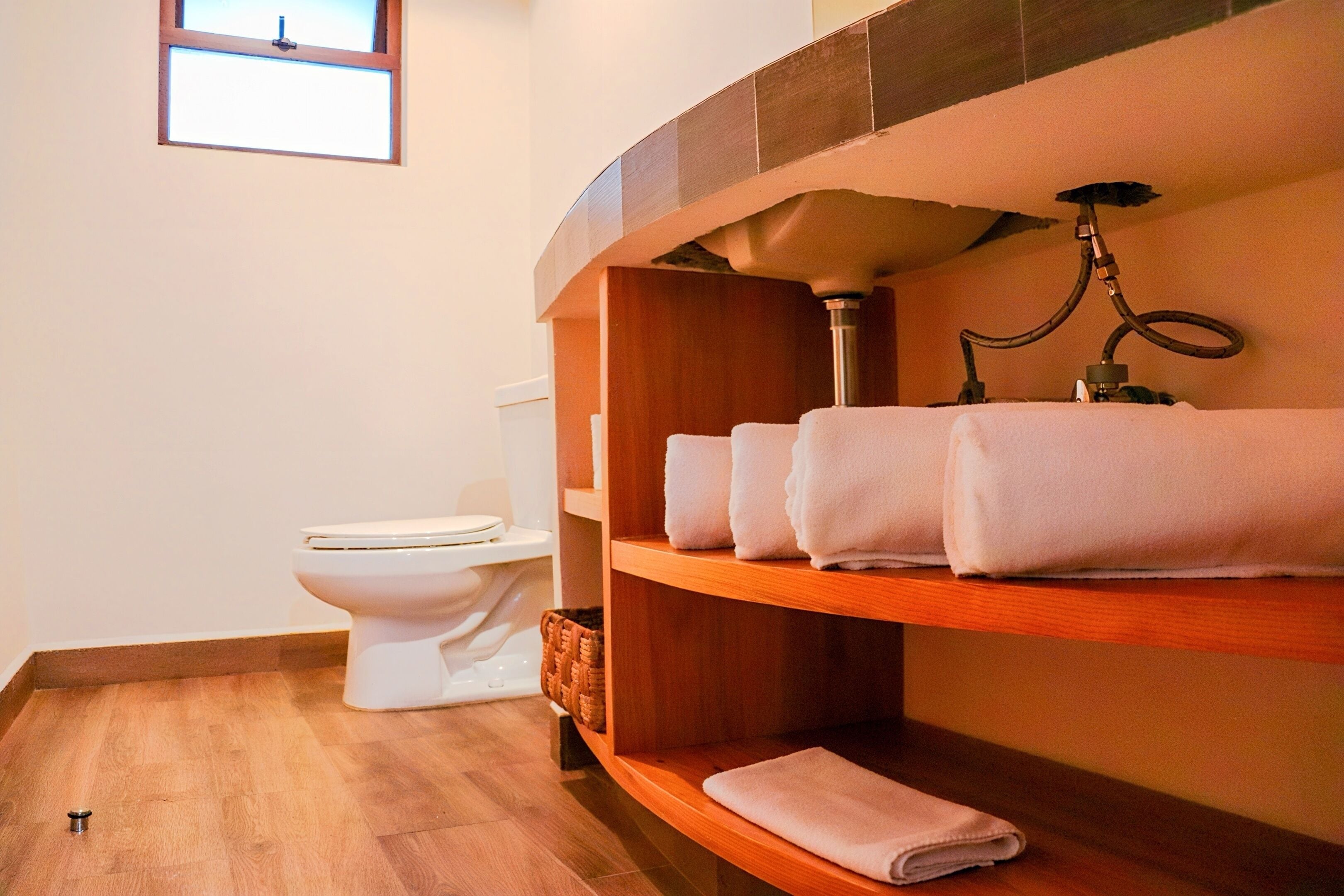 Une salle de bain avec des toilettes, une étagère avec des serviettes pliées et une fenêtre.