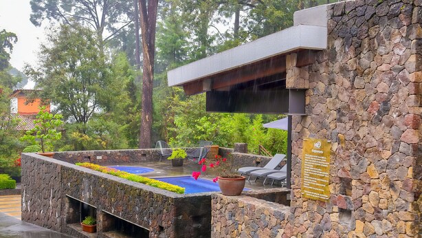 Un espacio al aire libre con paredes de piedra, una piscina, sillas de descanso y un letrero que indica una cámara de alta definición.
