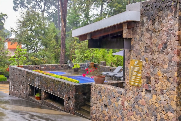 Un espacio al aire libre con paredes de piedra, una piscina, sillas de descanso y un letrero que indica una cámara de alta definición.