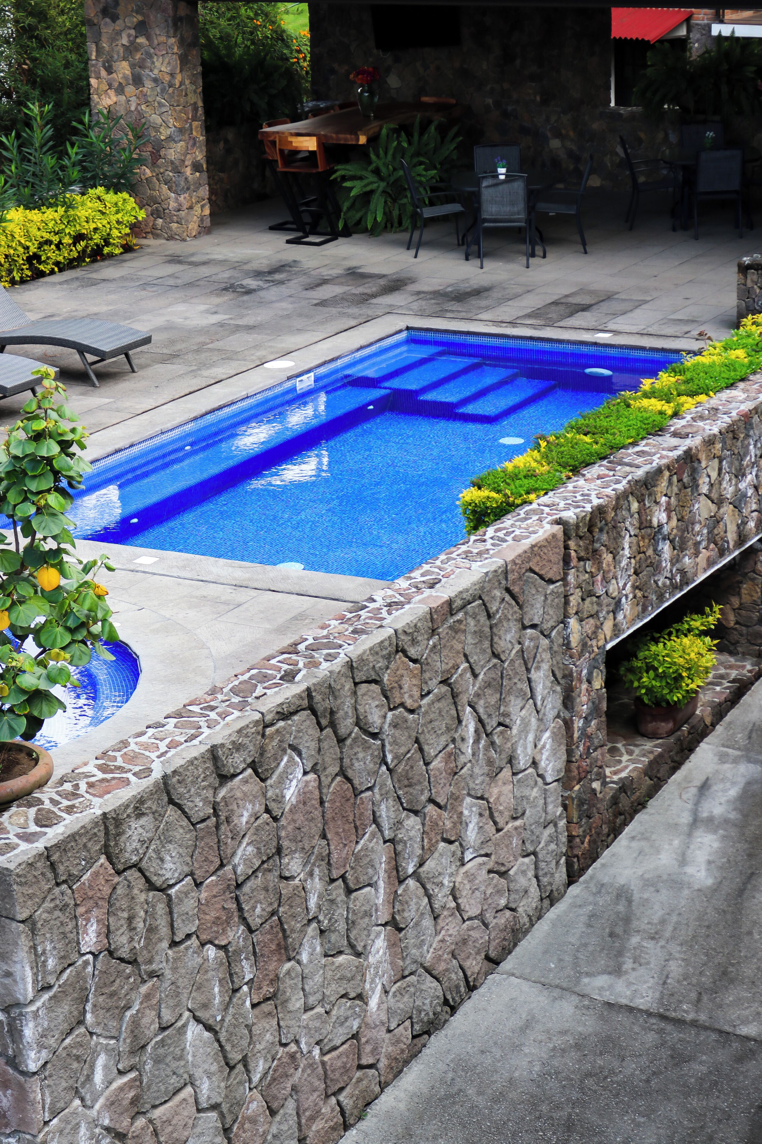 A swimming pool with stone walls and a patio area with outdoor furniture.