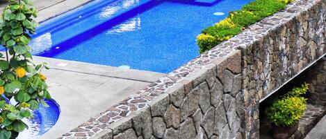Piscina com paredes de pedra e um espaço de estar ao ar livre com móveis de jardim.