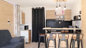 En kompakt opholdsstue med sofa, spisebord med barstole, et tekøkken og et fjernsyn.
