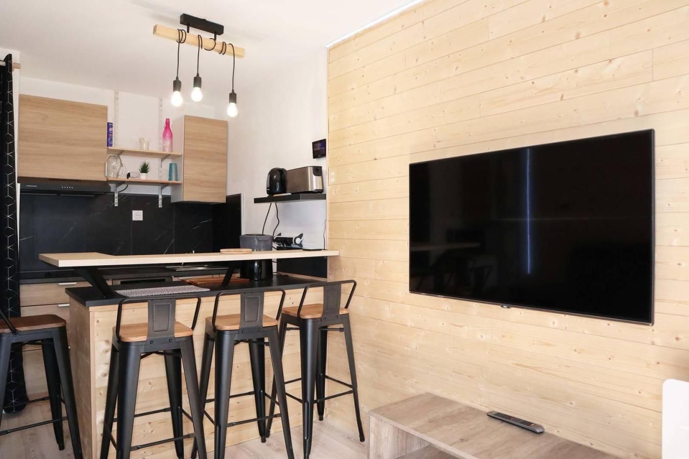 A modern kitchen with a large flat-screen TV, wooden cabinets, and a bar area with stools.