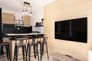 A modern kitchen with a large flat-screen TV, wooden cabinets, and a bar area with stools. - 20m from ski slopes, 8th floor, balcony, tv, 25m², Les Orres (Les Orres)