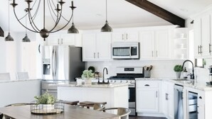 A modern kitchen with white cabinets, a central island, and a dining area with a wooden table and metal chairs. - Family Flagstaff Retreat  Sleeps 12 Mountain Views  EV Charger  Near NAU with AC (Flagstaff)