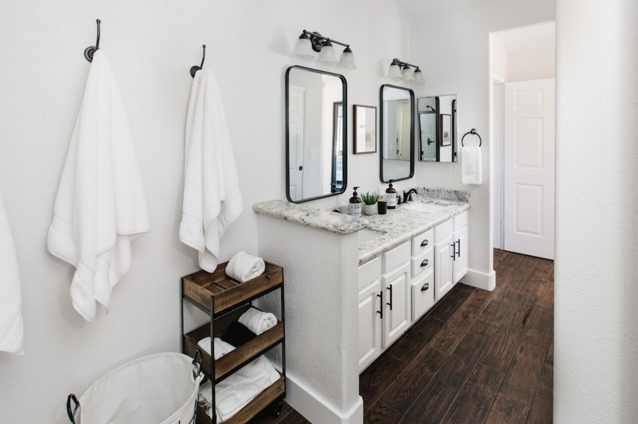 A modern bathroom with white walls, a marble countertop, and a wooden floor.