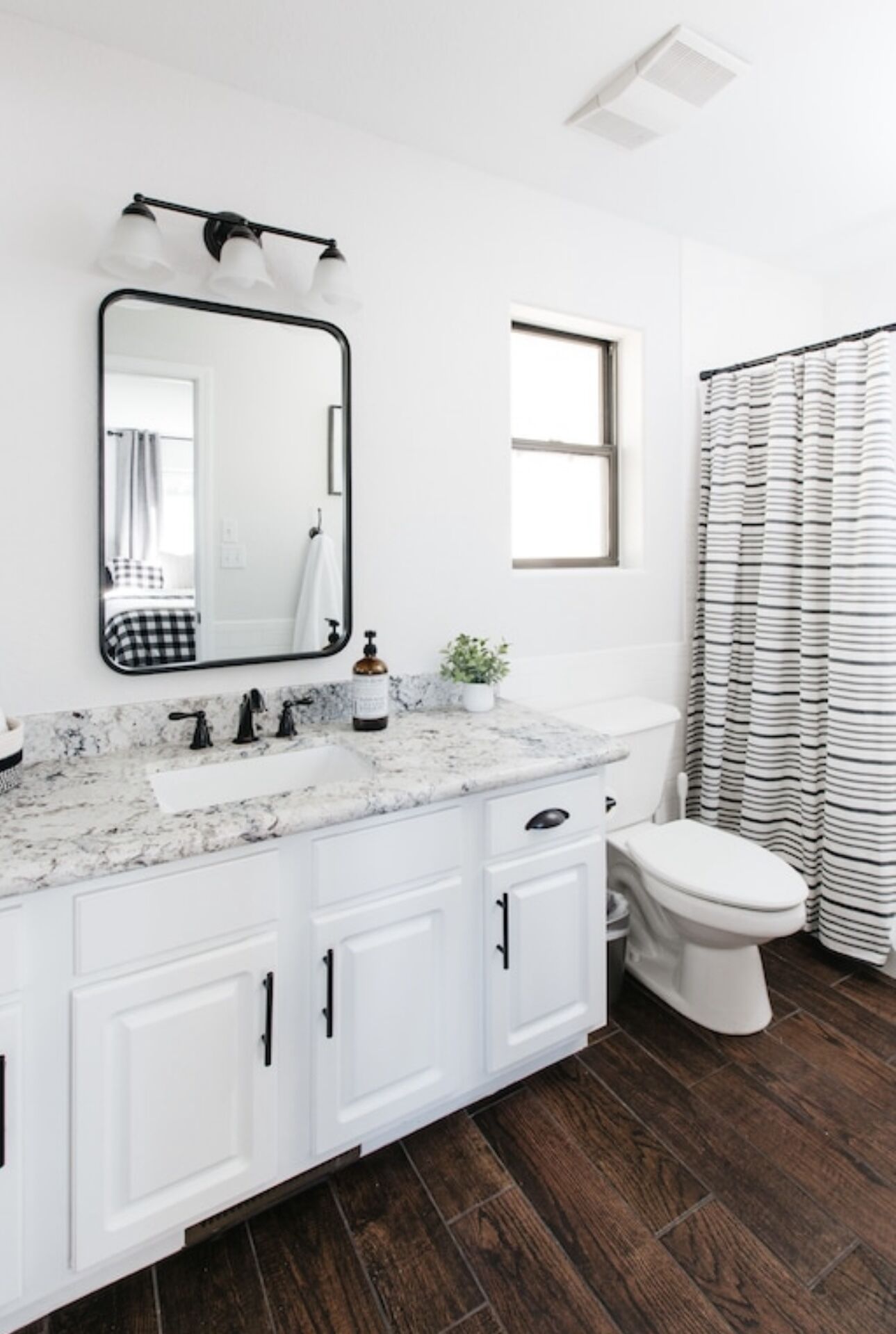 A bathroom with a white vanity, a large mirror, a toilet, and a striped shower curtain.