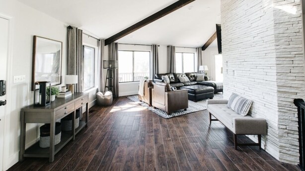 A modern living room with a dark wood floor, a grey sofa, a white stone accent wall, and a large window providing natural light. - Family Flagstaff Retreat  Sleeps 12 Mountain Views  EV Charger  Near NAU with AC (Flagstaff)
