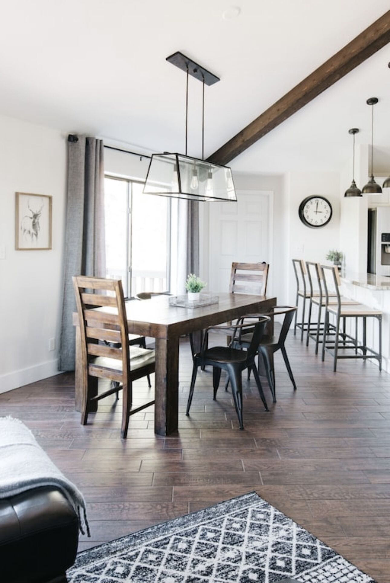 A dining area with a wooden table and chairs, a hanging light fixture, and a patterned rug.