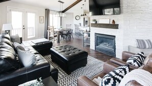 A modern living room with a fireplace, leather sofas, and a dining area. - Family Flagstaff Retreat  Sleeps 12 Mountain Views  EV Charger  Near NAU with AC (Flagstaff)