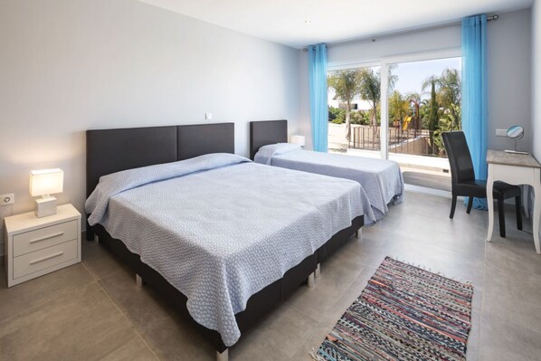 A hotel room with two beds, a desk, a chair, a nightstand, and a view of the outdoors.