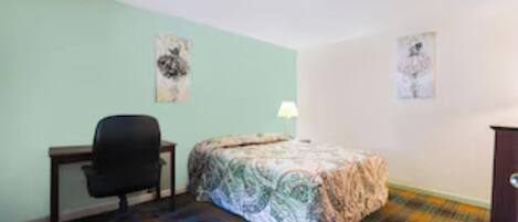 A room with a bed, a desk, and a chair. There are two wall-mounted artworks.