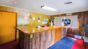 A hotel room with a wooden reception desk, a television, and a small seating area with a red rug. - Travelers Inn by OYO Beaver, Hwy 19 (Beaver)
