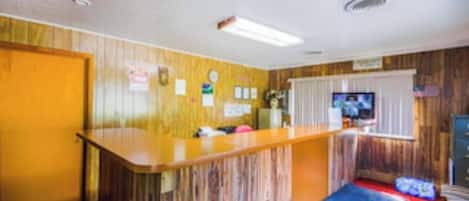 Une chambre d’hôtel avec un comptoir d’accueil en bois, une télévision et un petit coin salon agrémenté d’un tapis rouge.