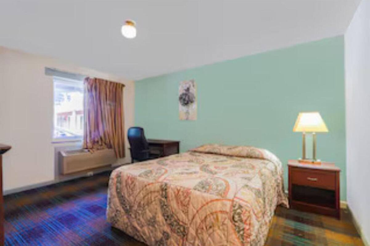 A hotel room with a bed, a chair, a desk, a lamp, and a window with curtains.
