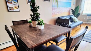 Ein Essbereich mit einem Holztisch, schwarzen Stühlen, einem kleinen Topfpflanzen und gerahmten Bildern an der Wand.