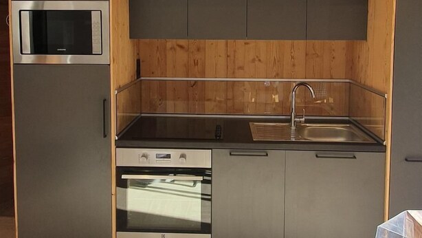 Una cucina compatta con mobili in legno, un forno a microonde integrato, un piano cottura in acciaio inossidabile e un lavandino.