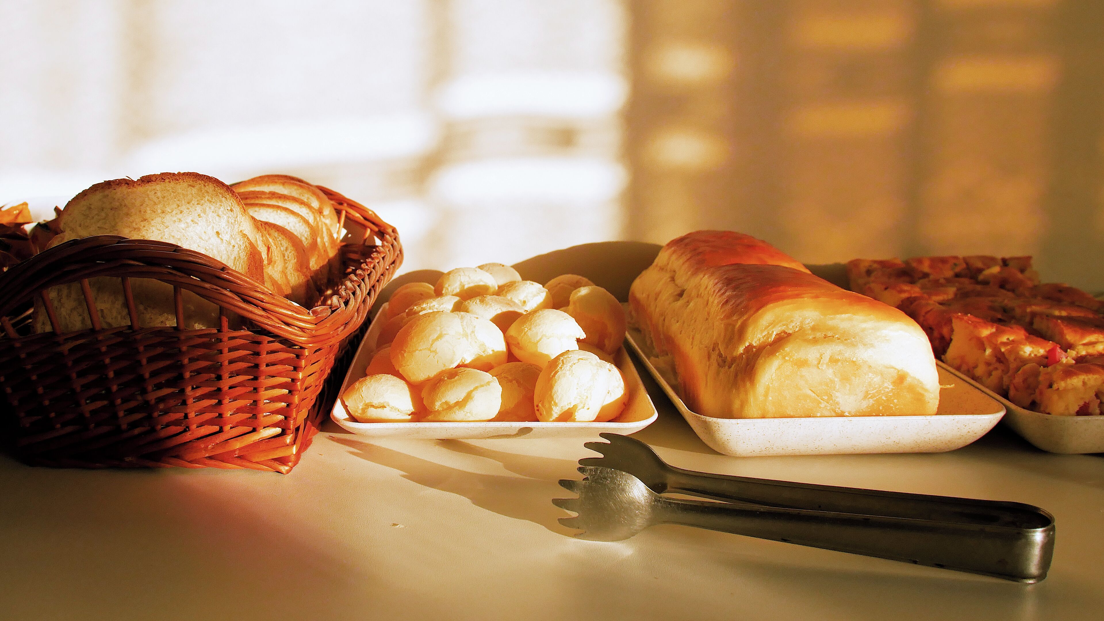 Diversos pães e doces sobre uma mesa, incluindo uma cesta de vime, uma bandeja e um pão.