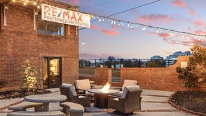 An outdoor patio with a fire pit, wicker furniture, and a brick building with a sign reading "REZMAX PREFERRED PROPERTIES". - Funky, Fun, and Fabulous!!! (Knoxville)