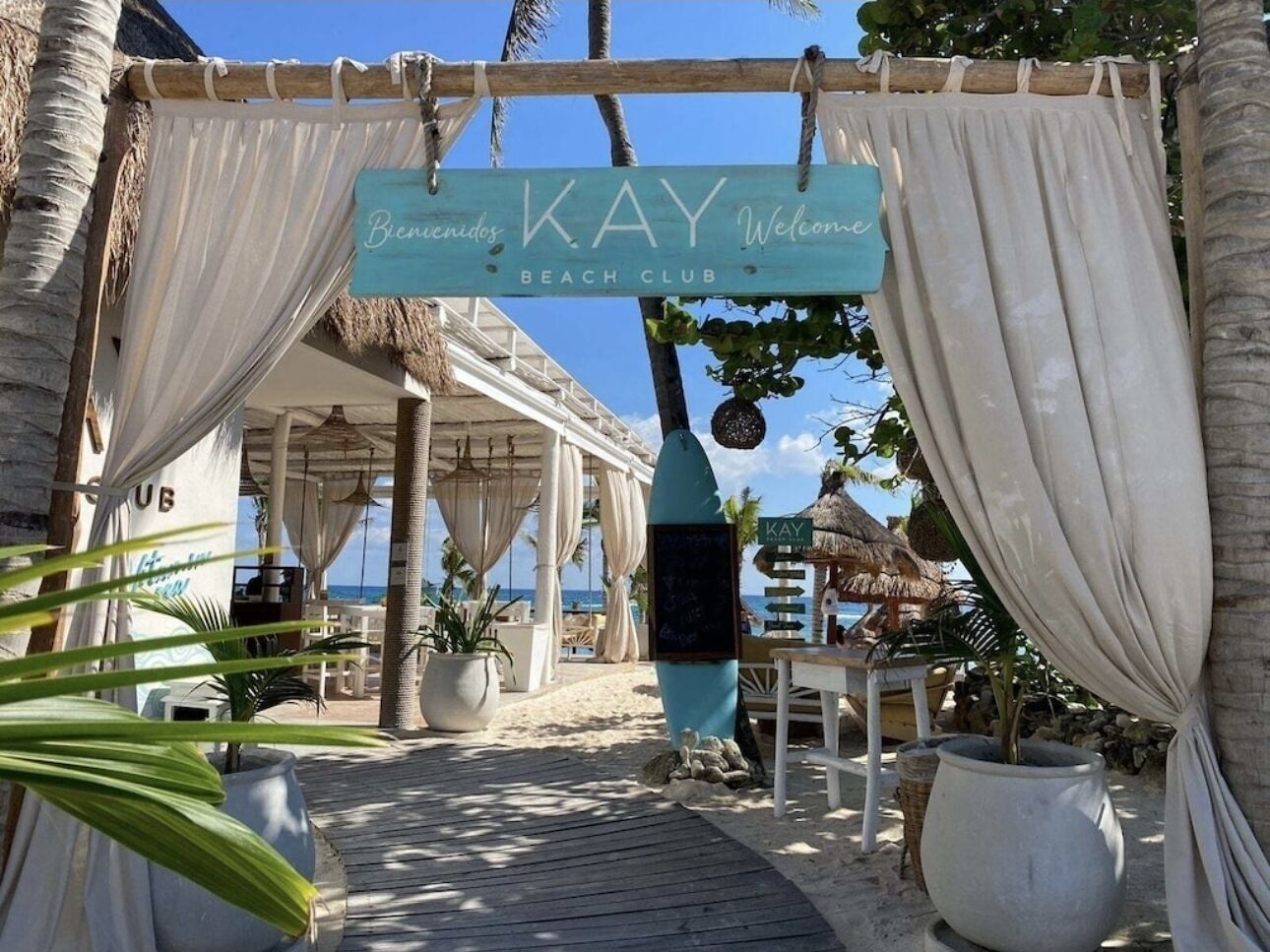 En entré till en strandklubb med en skylt som visar texten: ”Välkomna till KAY Beach Club”.