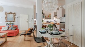 A modern living room with a red sofa, a dining table set with plates and glasses, and a kitchen in the background.